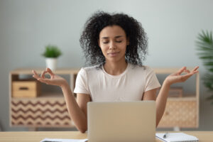Woman meditating at desk with open laptop